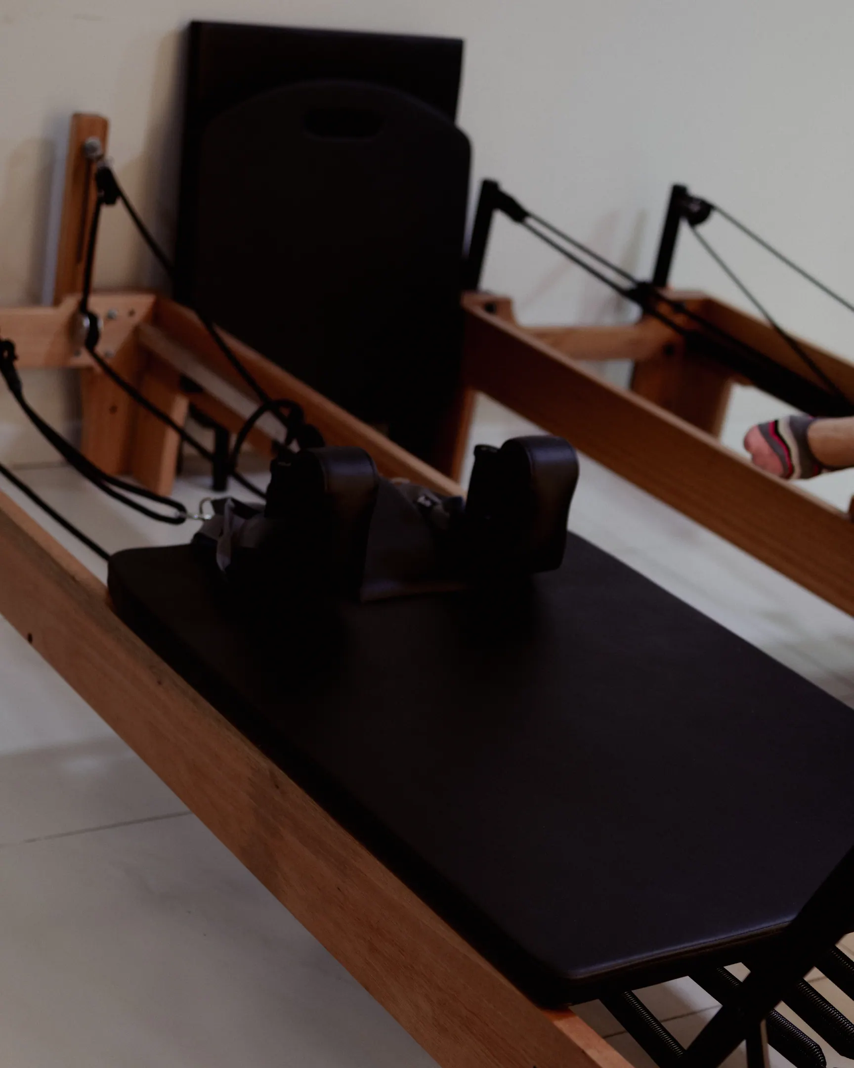 Aparelho de pilates reformer de madeira e estofado preto, visto de perto e vazio, na sala clara do estúdio