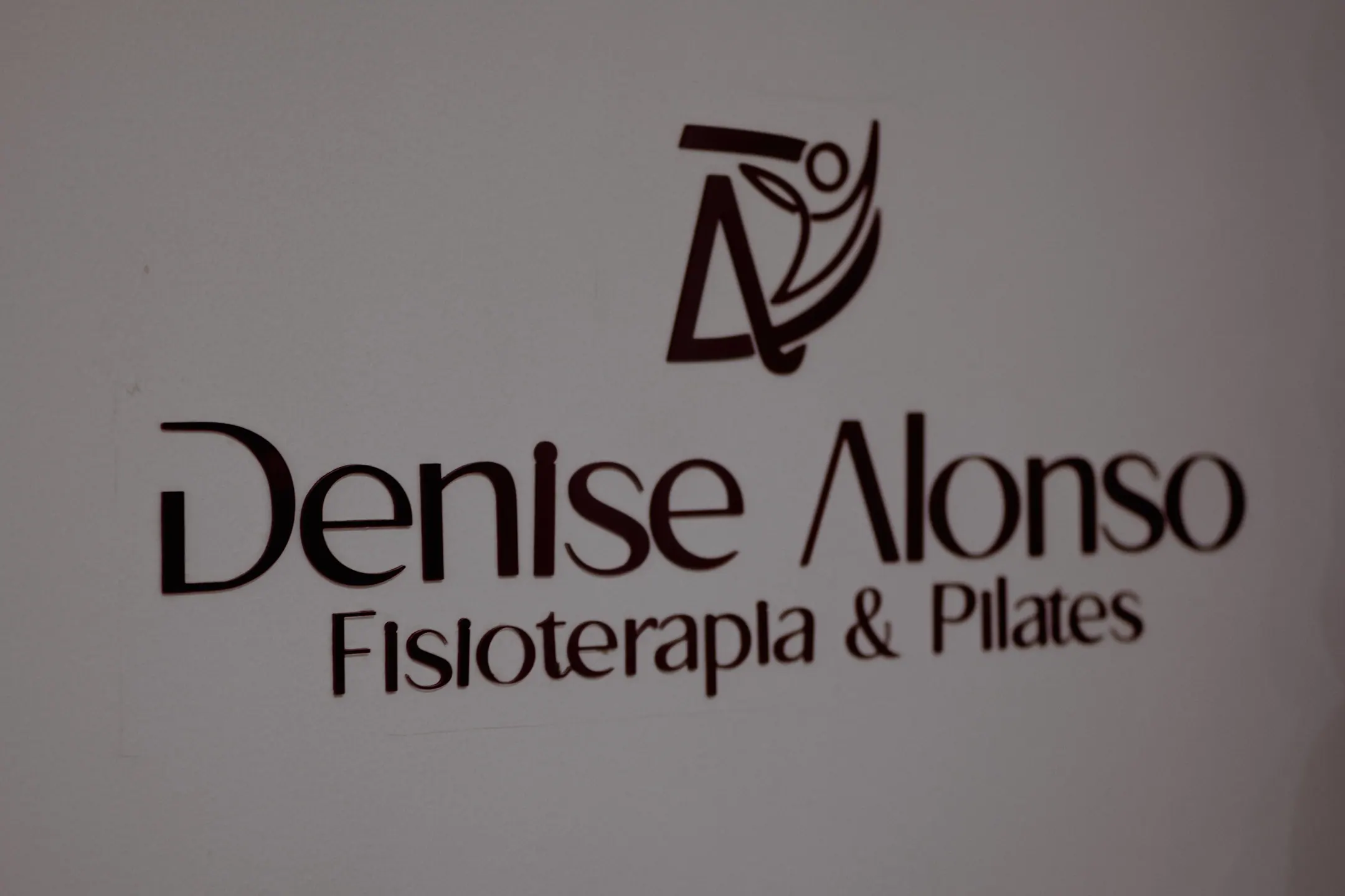 Logo em relevo na parede branca com o nome Denise Alonso, fisioterapia e pilates