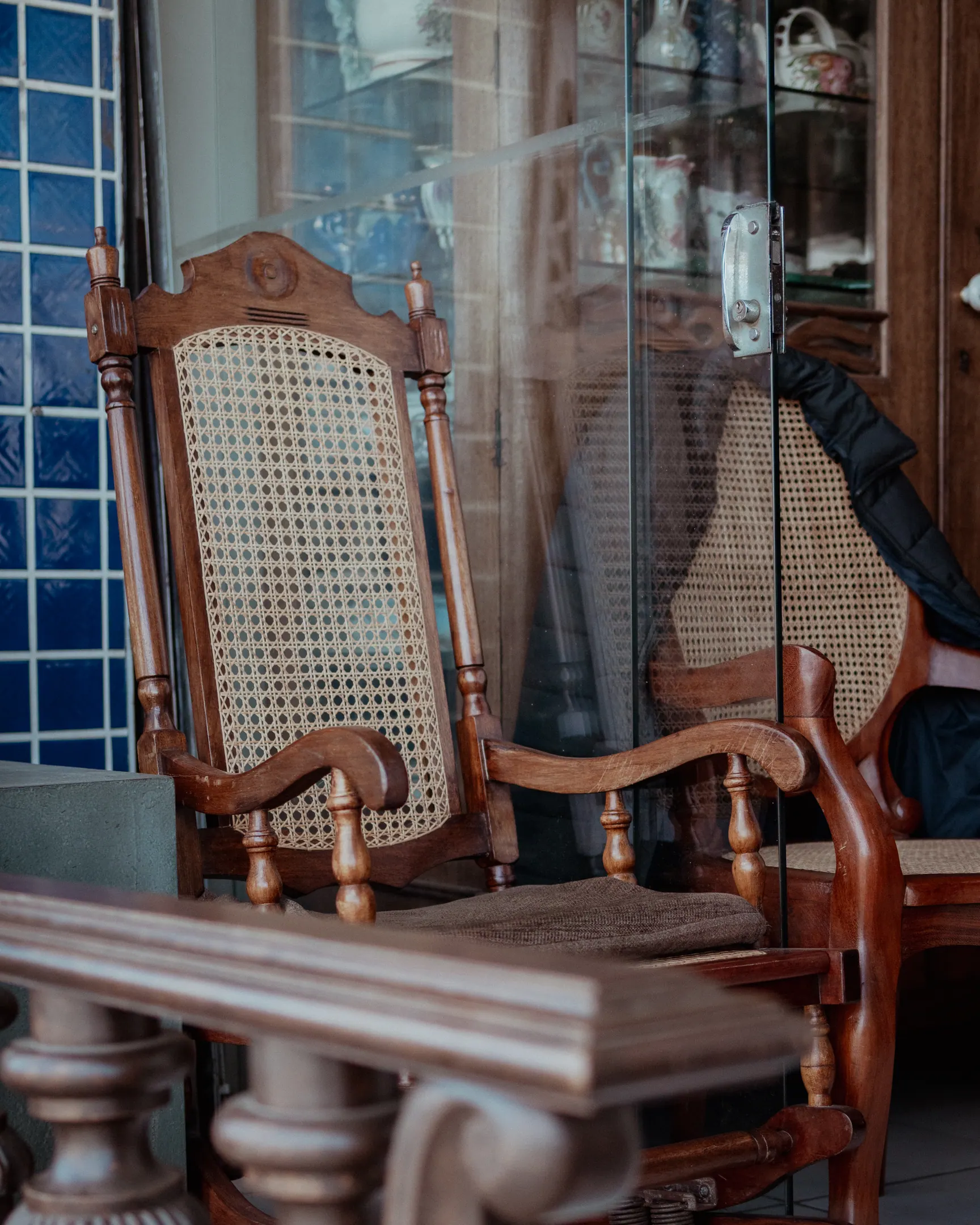 Cadeira de balanço de palhinha e mesa de jacarandá entalhada, ao lado de uma vitrine envidraçada