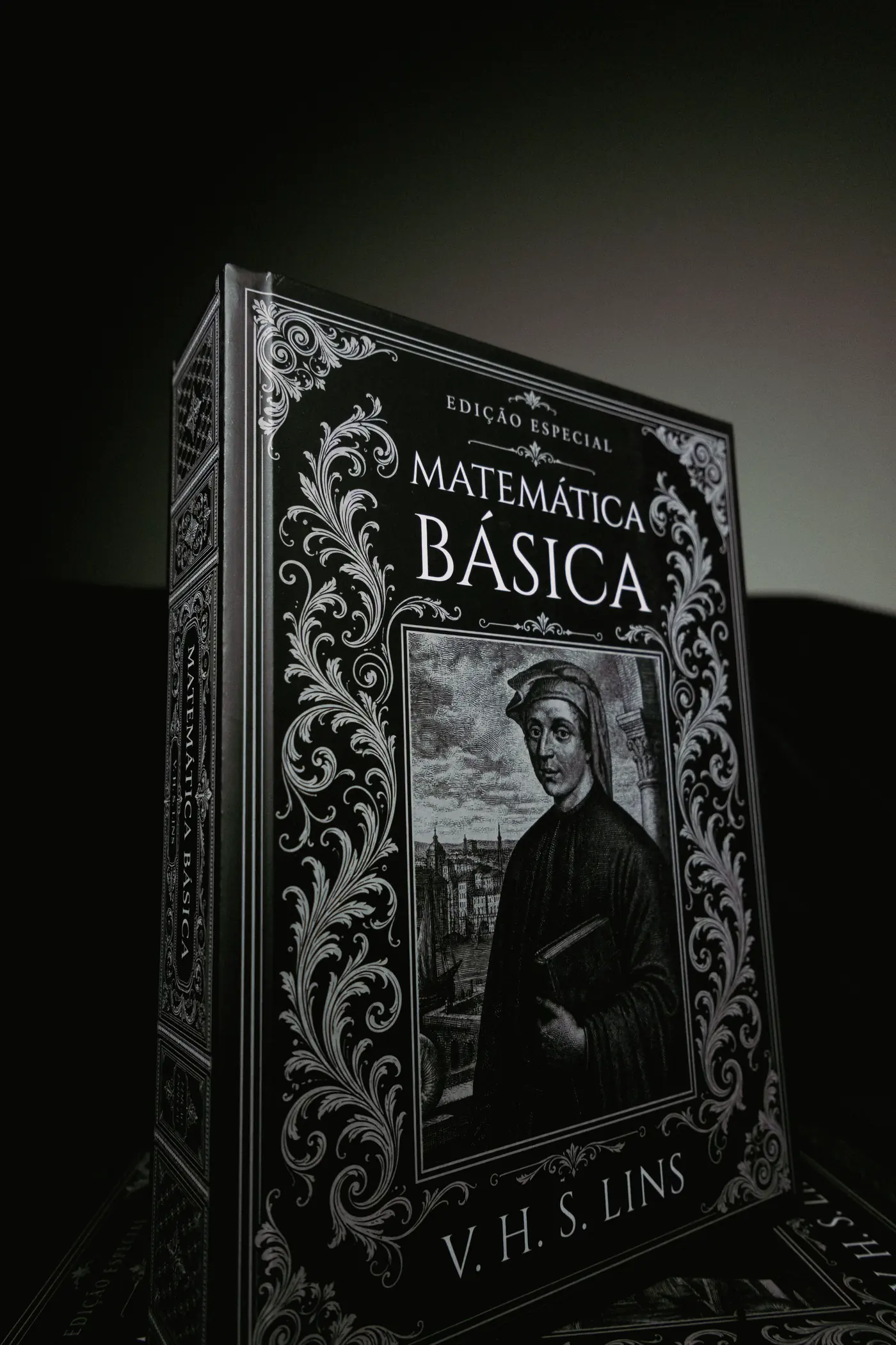 Livro Matemática Básica em capa dura, iluminado por uma única fonte de luz sobre fundo escuro
