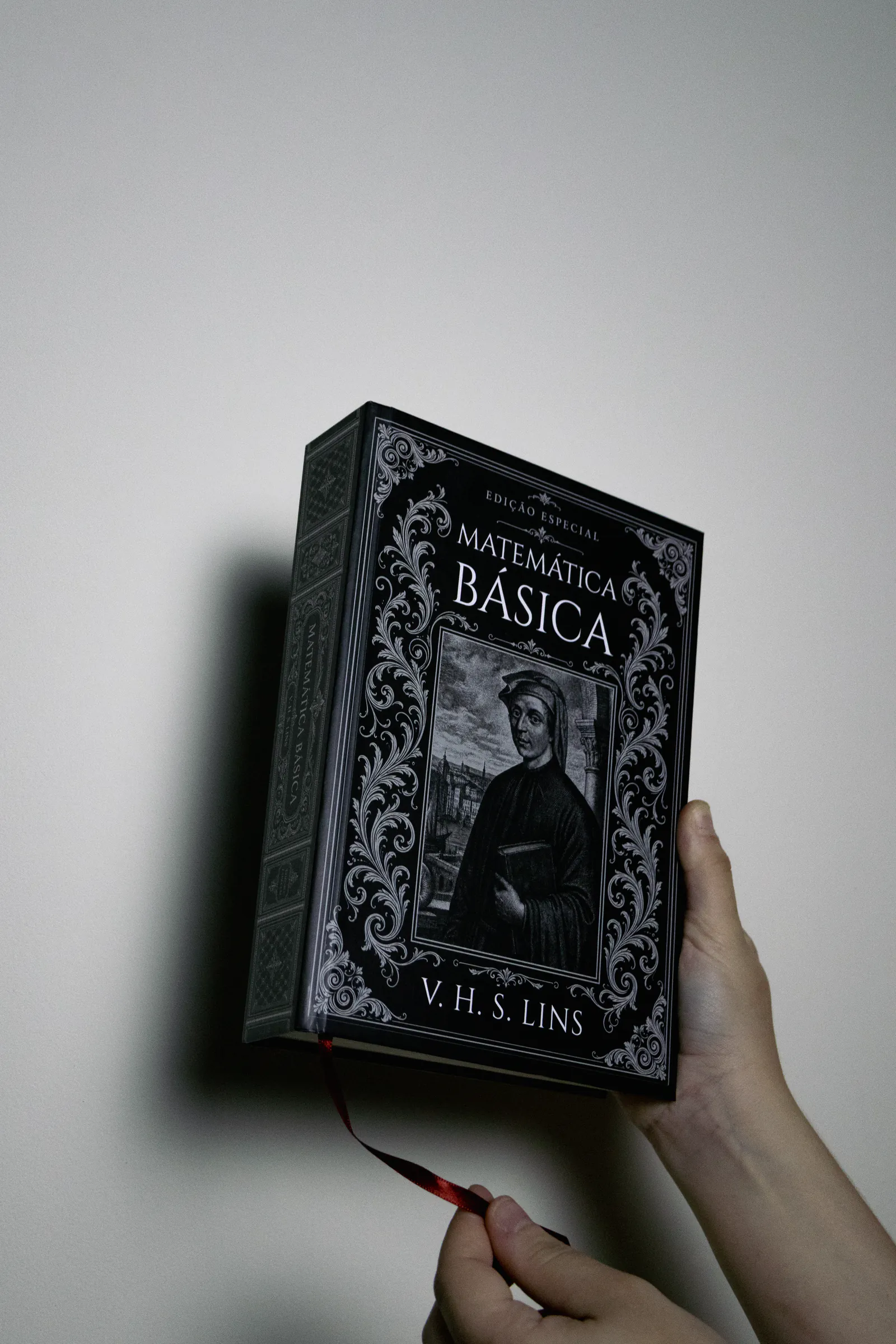 Livro segurado na mão contra fundo claro de estúdio, com a fita marcadora à mostra