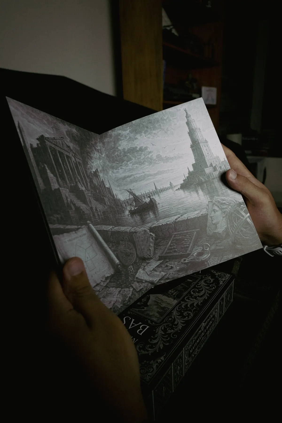 Mãos abrindo o livro numa página de gravura em preto e branco