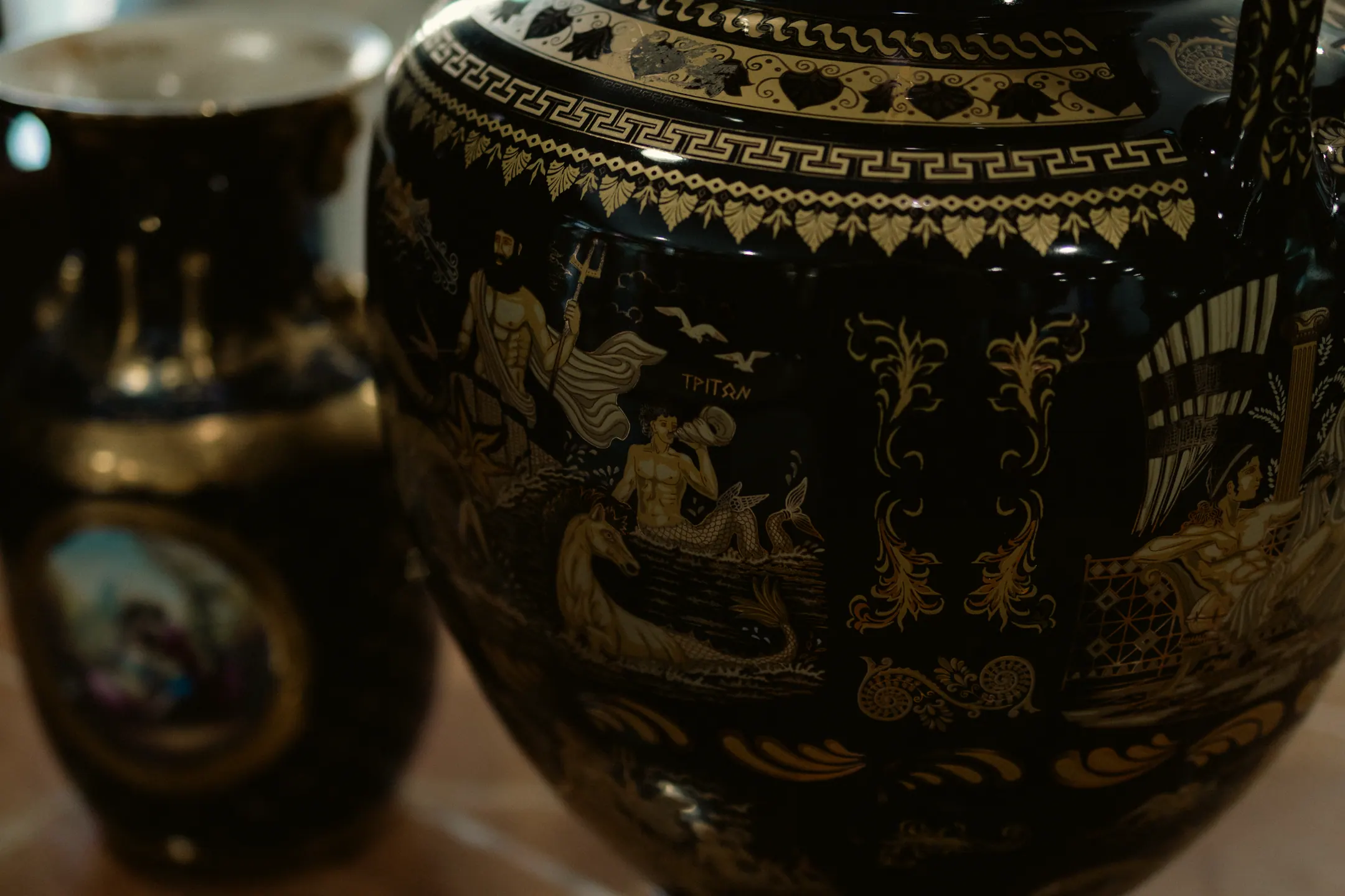 Vaso de cerâmica preta com cena mitológica pintada em dourado, em close, sobre a bancada da loja
