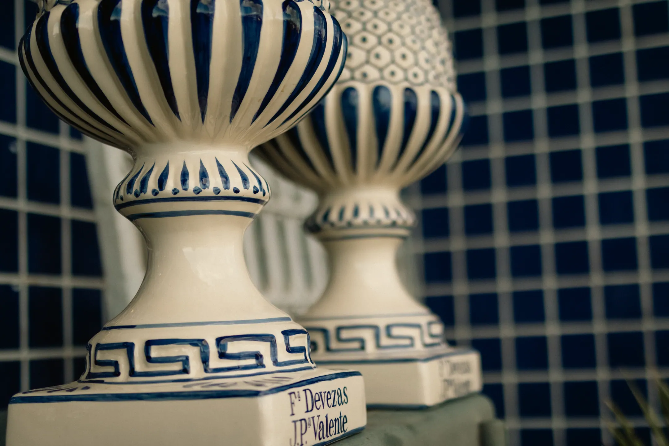 Par de vasos de faiança branca com friso azul em relevo, diante de uma parede de azulejos azuis