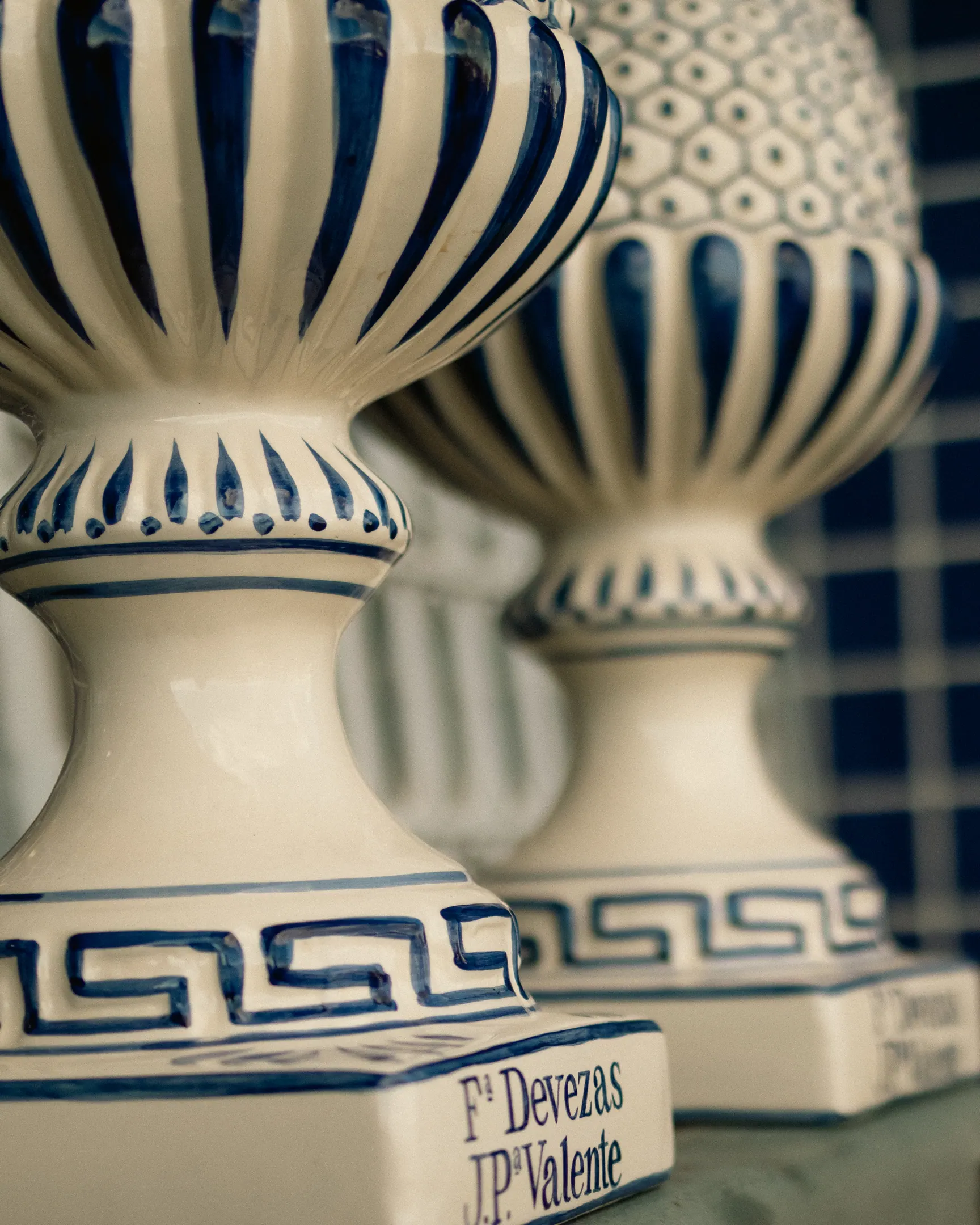 Par de vasos de faiança branca com friso azul em relevo, diante de uma parede de azulejos azuis