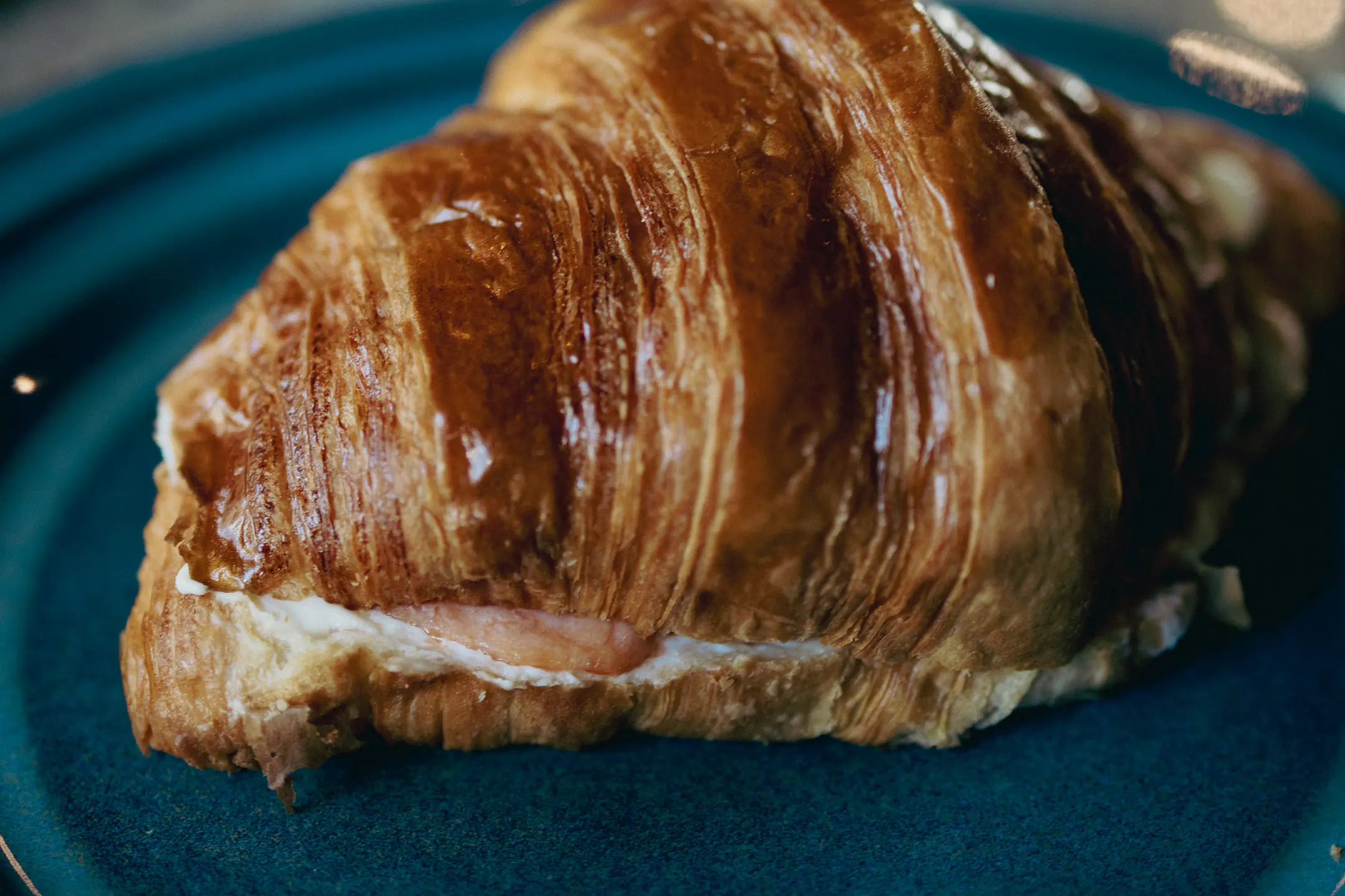 Croissant recheado, dourado e folhado, servido num prato de cerâmica azul