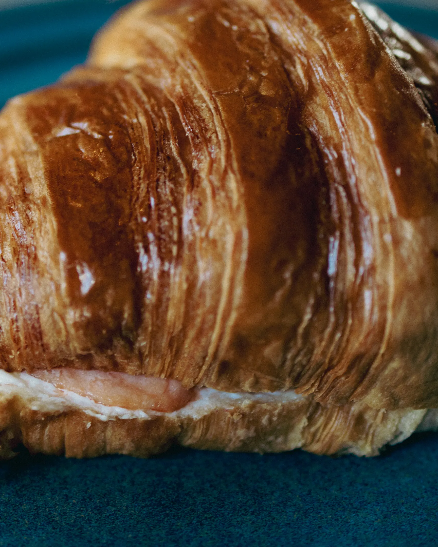 Croissant recheado, dourado e folhado, servido num prato de cerâmica azul