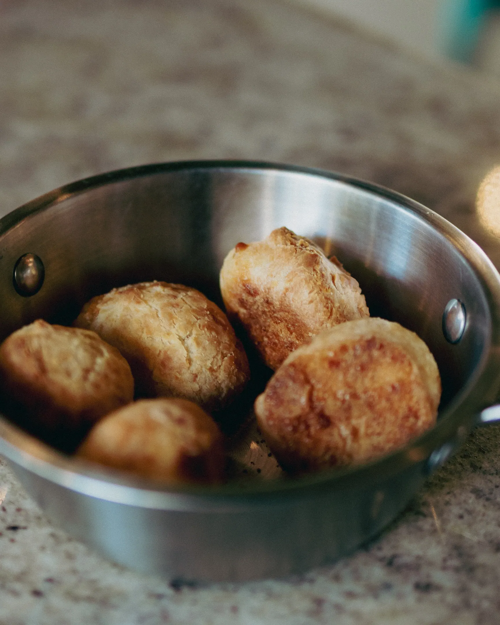 Bolinhos fritos dourados servidos numa frigideira pequena de metal sobre a mesa de granito