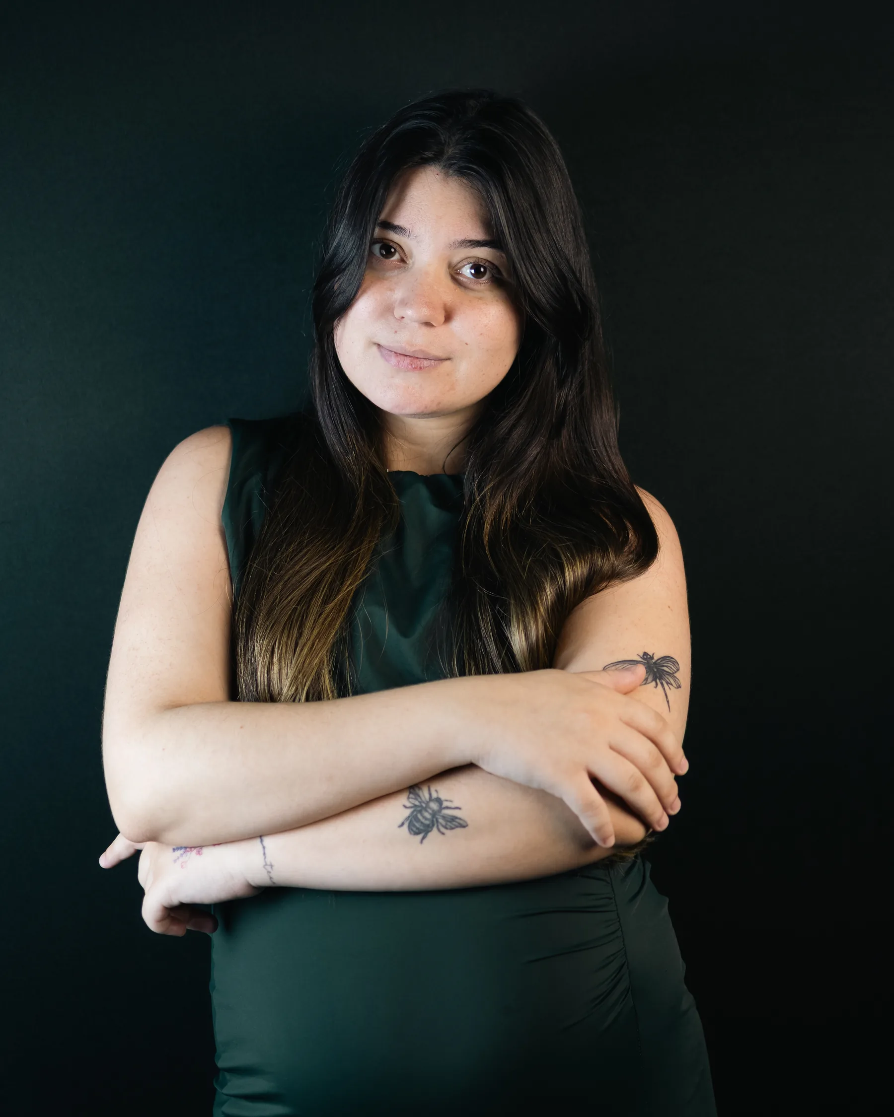 Retrato de estúdio de corpo até a cintura: a mesma mulher de braços cruzados, de frente para a câmera, sobre fundo verde-escuro