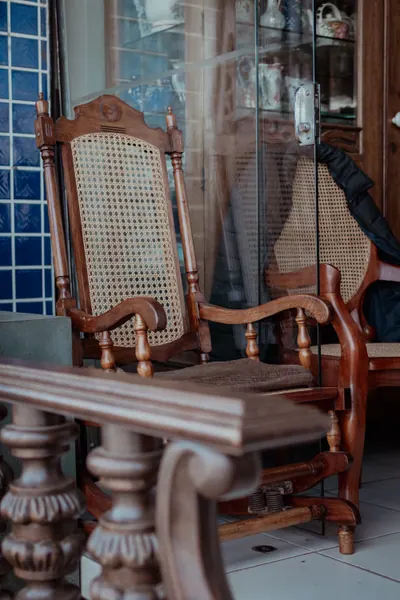 Cadeira de balanço de palhinha e mesa entalhada, ao lado de uma vitrine envidraçada