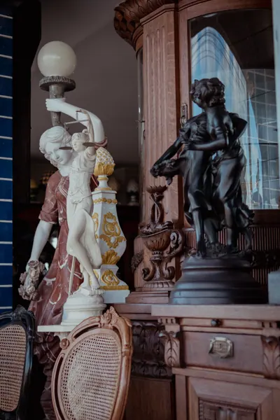 Salão da loja com luminária de figura feminina, cadeiras de palhinha e móvel entalhado