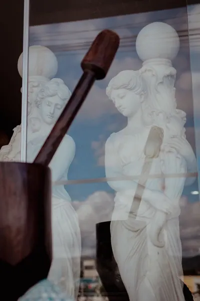 Duas figuras de mármore vistas através do vidro da vitrine, com o céu refletido
