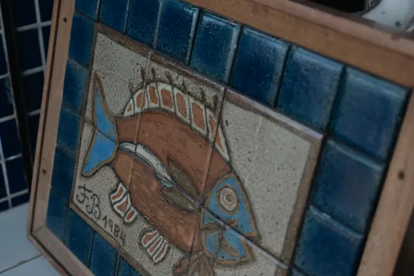 Painel de azulejos com um peixe pintado, apoiado na parede de azulejo azul