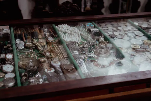 Vitrine iluminada com joias, colares de pérola, relógios e moedas