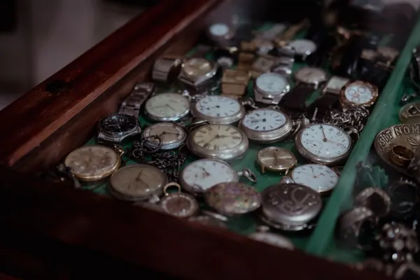 Vitrine de madeira aberta com dezenas de relógios de bolso sobre feltro verde