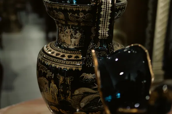 Vaso negro com cena de peixes dourados, ao lado de outra peça