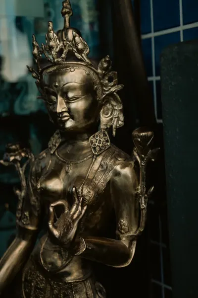 Estátua de bronze de uma figura sentada, com a mão em gesto de bênção
