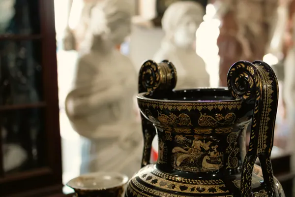 Vaso negro em primeiro plano, com as estátuas de mármore desfocadas atrás