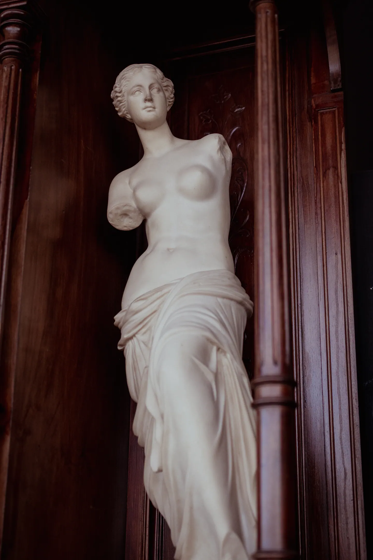 Réplica da Vênus de Milo em mármore branco, entre colunas de madeira