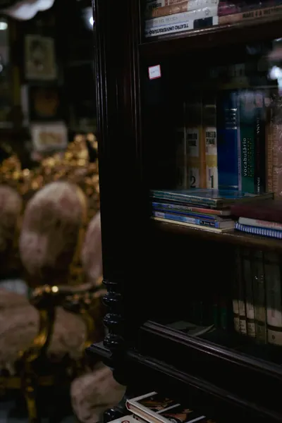 A poltrona dourada e a estante de livros atrás, na penumbra
