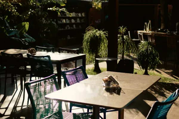 Mesas de granito e cadeiras de fio no sol da tarde, com o jardim ao fundo