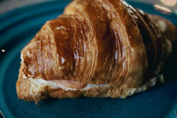 Croissant recheado, dourado e folhado, servido num prato de cerâmica azul