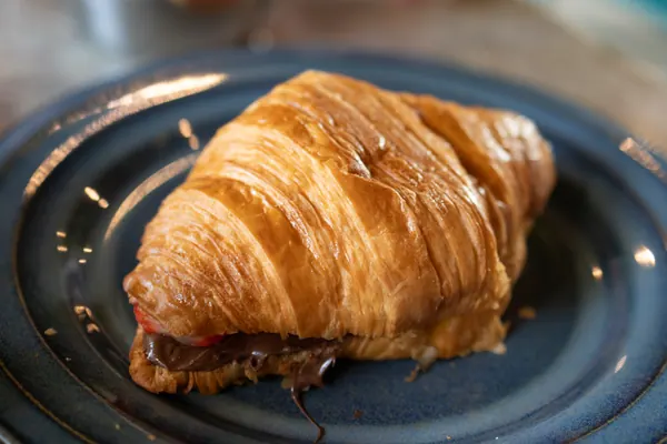 Croissant com recheio escuro e morango, num prato azul de borda alta