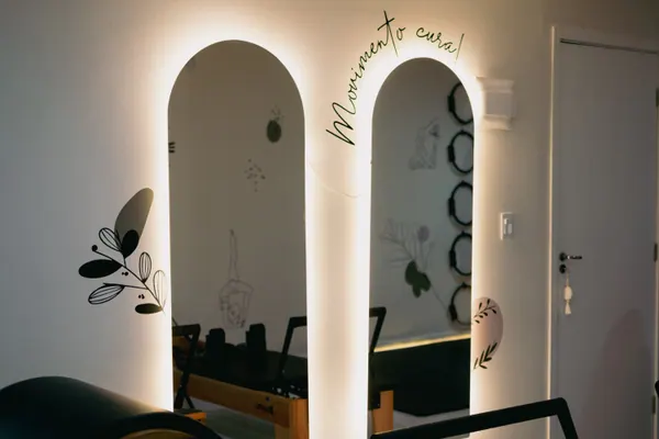 Dois vãos em arco iluminados por trás na parede branca, com a frase Movimento cura em cursiva