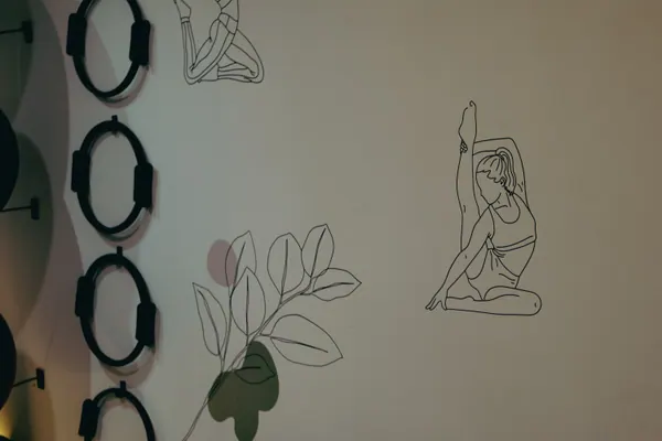 Parede com desenhos de linha de figuras em pose de pilates, entre arcos flexíveis