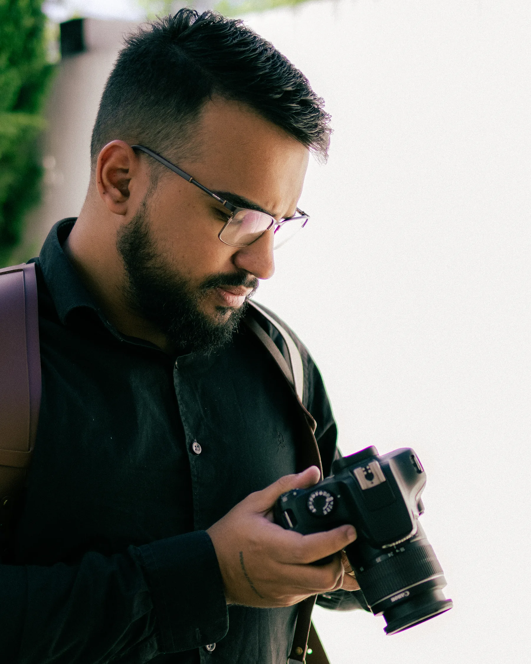 Victor Lins em pé, de camisa preta, conferindo a foto no visor da câmera em luz natural
